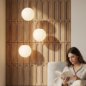 May include: Three spherical pendant lights with a warm glow hang from the ceiling. The lights are suspended in front of a wooden wall panel with a repeating vertical design. A person is sitting on a bed reading a book.