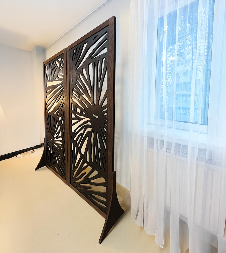May include: A brown wooden room divider with a decorative cutout design. The divider is made of two panels, each with a different pattern. The panels are connected by a hinge.