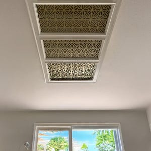 May include: Three white ceiling panels with a gold geometric pattern. The panels are arranged in a row and are set against a white ceiling.