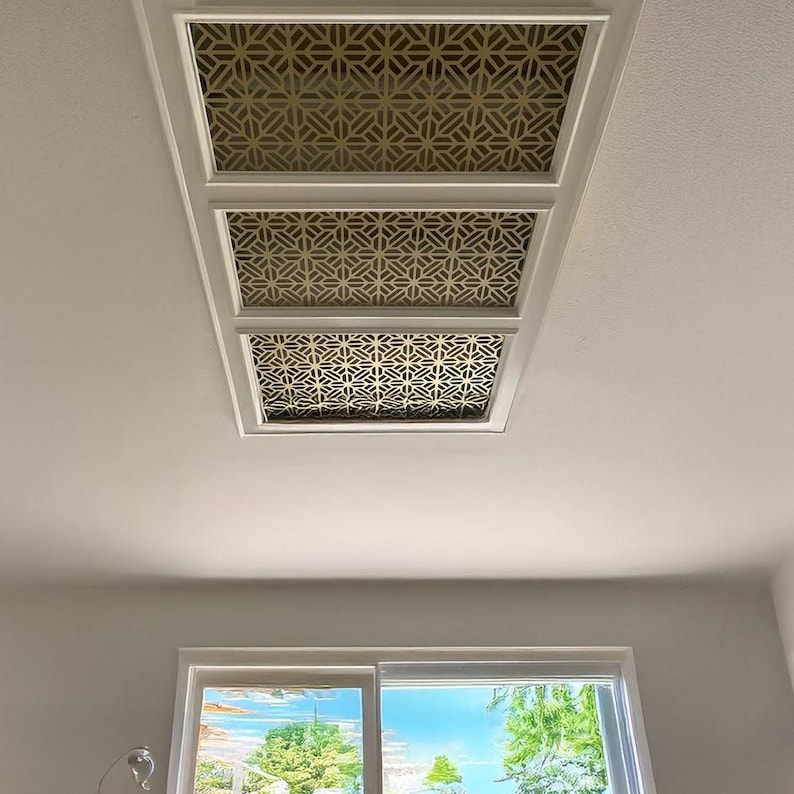 May include: Three white ceiling panels with a gold geometric pattern. The panels are arranged in a row and are set against a white ceiling.