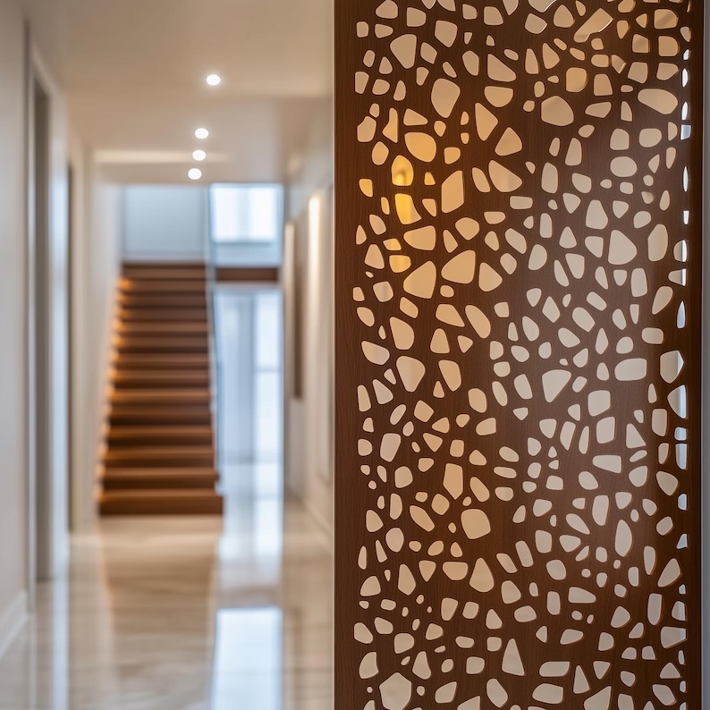 Close-up of a wooden decorative screen with organic cut-out pattern, placed in a modern hallway with recessed lighting and a floating staircase.