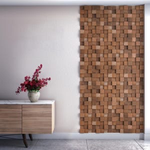 May include: A wall panel featuring a three-dimensional grid of square wooden blocks in varying shades of brown. The panel is mounted on a wall next to a wooden cabinet with a white top, which holds a vase filled with dark pink flowers.