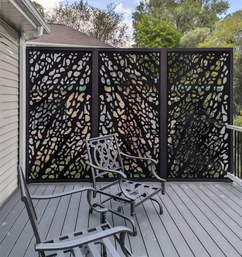 Pu&ograve; includere: Un paravento in metallo nero con un motivo organico ritagliato, installato su un terrazzo in legno. Due sedie in metallo sono di fronte allo schermo. Lo schermo &egrave; composto da tre pannelli, fornendo un elemento decorativo e funzionale.