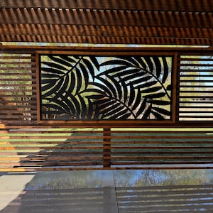 Outdoor pergola with a slatted wooden privacy screen featuring a tropical leaf cut-out design, casting shadows on the patio.