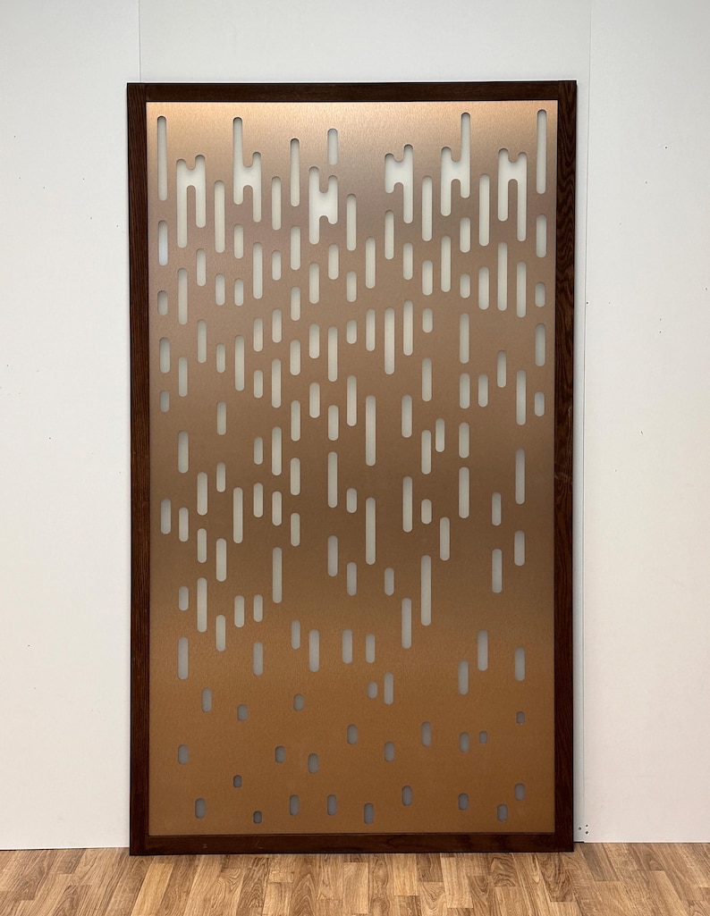 Pu&ograve; includere: Un pannello rettangolare color rame con una cornice in legno marrone scuro. Il pannello presenta un motivo di ritagli rettangolari verticali e arrotondati. Il design crea una texture visiva e permette il passaggio della luce, adatto per divisori o arte murale decorativa.