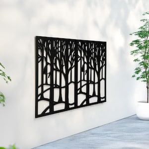 Pu&ograve; includere: Un'opera d'arte da parete in metallo nero raffigurante una scena di foresta. L'opera presenta una forma rettangolare con un design ritagliato di alberi e rami. Il pezzo &egrave; montato su un muro bianco, con uno scorcio di una pianta in un vaso bianco.