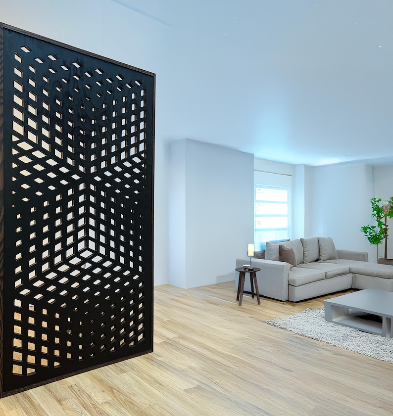 May include: A black room divider with a geometric pattern. The divider is made of wood and has a modern design. The divider is in front of a living room with a couch and a coffee table.