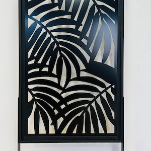 Pu&ograve; includere: Schermo decorativo in metallo nero con un design a foglie di palma ritagliate. Lo schermo rettangolare ha una cornice nera e poggia su due gambe in metallo nero. Il design crea un contrasto tra le foglie nere e lo sfondo.