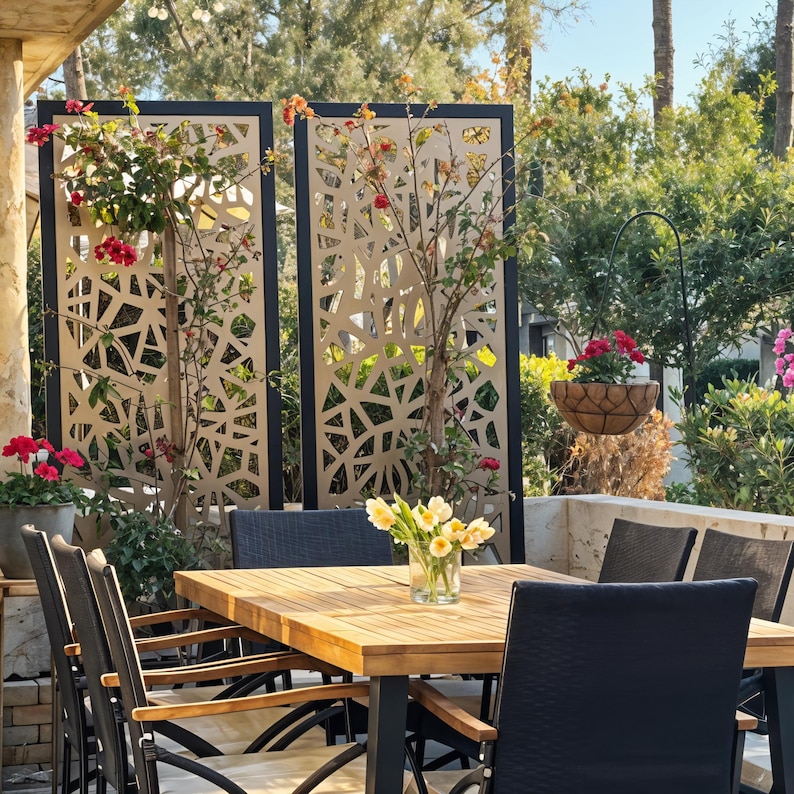 Outdoor dining area with a wooden table, black chairs, floral decor, and geometric privacy screens adorned with climbing plants.