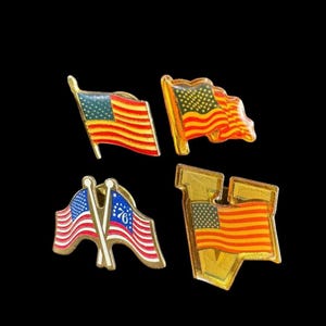 May include: Four vintage American flag pins. Each pin features a different design of the American flag, with red and yellow stripes and a blue field of stars. The pins are gold-toned and have a glossy finish.