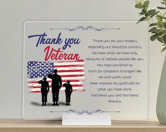 May include: A clear acrylic plaque with a white stand, featuring a red, white, and blue American flag with three silhouetted figures of soldiers saluting. The text "Thank you Veteran" is written in blue and white lettering. The plaque also includes a message of gratitude for veterans.