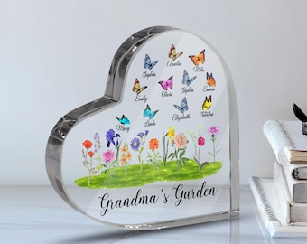 May include: A heart-shaped clear acrylic paperweight with a colorful garden scene and butterflies. The butterflies have names written on them, such as Amelia, Sophia, and Emma. The text at the bottom reads "Grandma's Garden".
