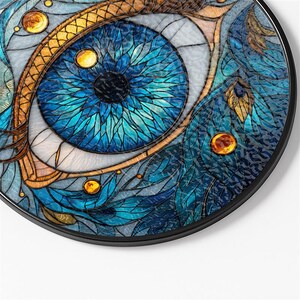May include: A round decorative piece featuring a stained-glass eye design. The eye has a blue iris with intricate details, surrounded by gold and brown accents. The piece includes a black border and small, round, amber-colored embellishments.
