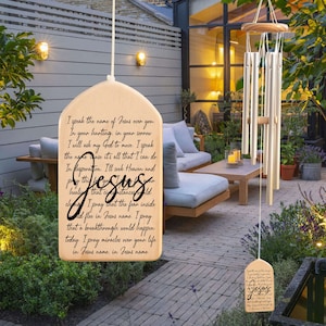 May include: Wooden wind chime with a rectangular plaque featuring a prayer to Jesus. The plaque is inscribed with the words "I speak the name of Jesus over you. In your hunting, in your sorrow I will ask my God to move. I speak the name cause it's all that I can do. In desperation. I'll seek Heaven and pray this Jesus..."