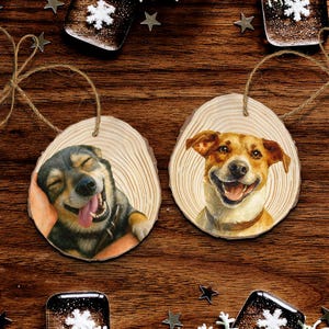 May include: Two wooden dog ornaments with a natural wood grain finish. Each ornament features a smiling dog portrait. One dog is black and gray, the other is tan and white. Both are strung with twine for hanging.