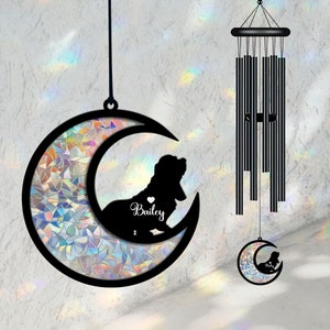 May include: Black metal wind chime with a crescent moon design featuring a silhouette of a dog and the name "Bailey". The moon is decorated with iridescent mosaic glass.
