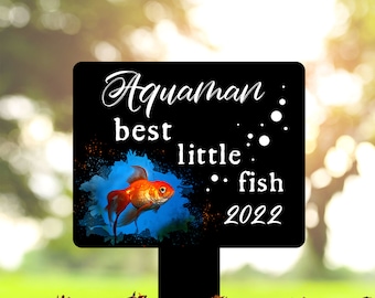 May include: Black metal garden stake with a blue and orange goldfish graphic. The text "Aquaman best little fish 2022" is written in white on the stake.