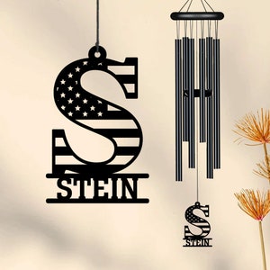 May include: Black metal wind chime with an American flag design. The chime features the letter "S" with the name "STEIN" below it. The chime is hanging from a black cord.