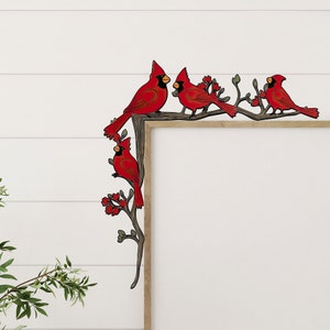 May include: Four red cardinal birds perched on a branch with green leaves. The birds are facing different directions and have black eyes and beaks. The branch is against a white wood panel background.