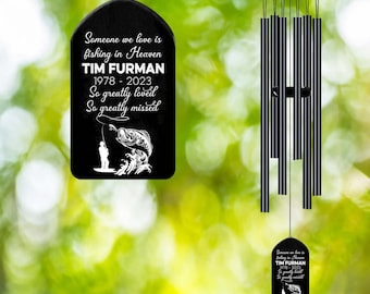 May include: Black wind chime with a black metal plaque that reads "Someone we love is fishing in Heaven TIM FURMAN 1978 - 2023 So greatly loved So greatly missed". The plaque features a silhouette of a person fishing with a fish jumping out of the water.