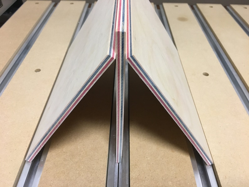 May include: Two pieces of wood with red, blue, and white stripes are joined together at a 90-degree angle. The wood is clamped to a table with a metal track.