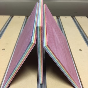 Pode incluir: Duas pe&ccedil;as de folheado de madeira, cada uma com m&uacute;ltiplas camadas de madeira de diferentes cores, est&atilde;o empilhadas uma em cima da outra. A madeira &eacute; um arco-&iacute;ris de cores, incluindo vermelho, laranja, amarelo, verde, azul e roxo.