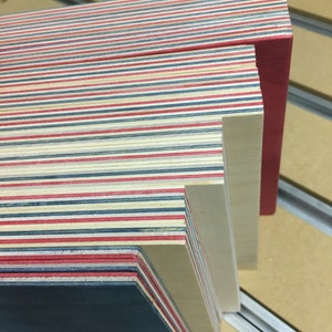 May include: A stack of thin wooden boards with alternating red, blue, and white stripes. The top board is a solid red color. The boards are stacked on a light brown surface.