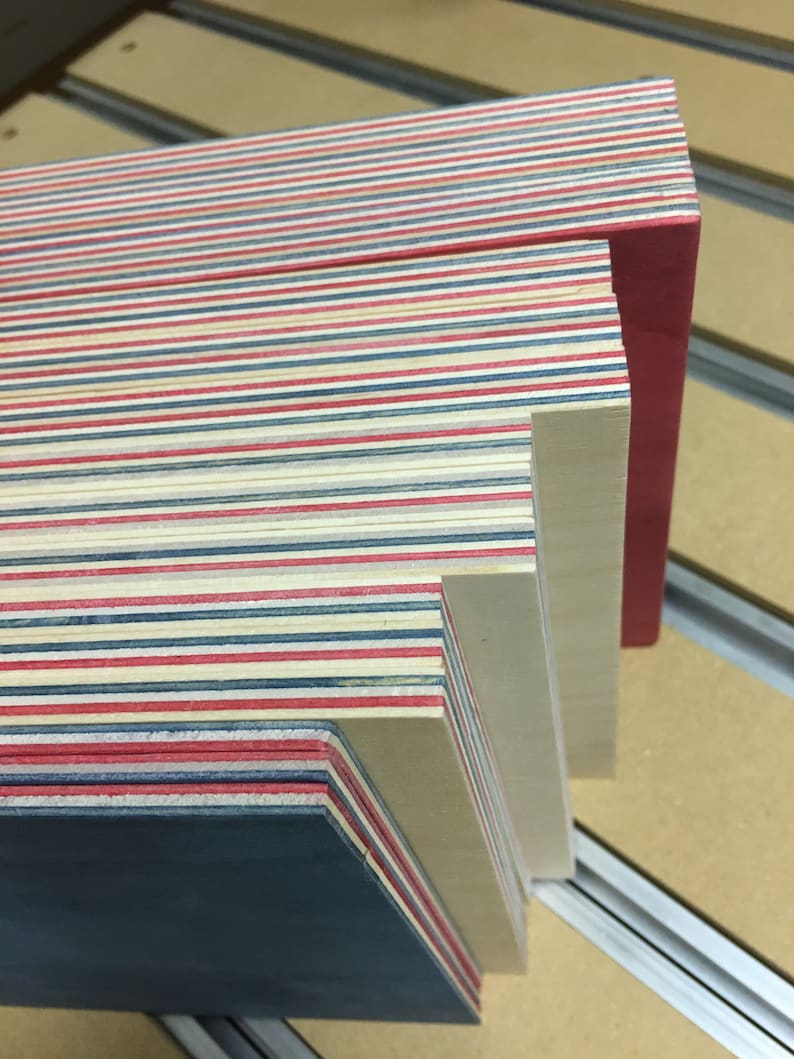 May include: A stack of thin wooden boards with alternating red, blue, and white stripes. The top board is a solid red color. The boards are stacked on a light brown surface.