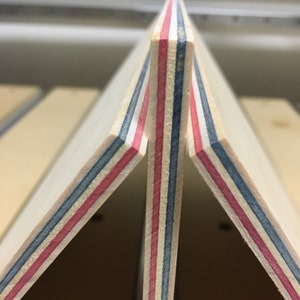 May include: Close-up of three pieces of wood veneer with red, blue, and white stripes. The wood is stacked on top of each other, creating a triangular shape.