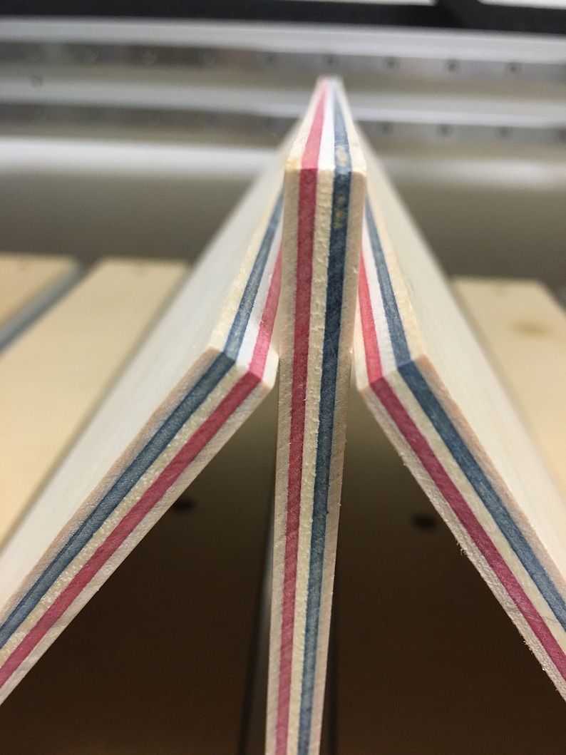 May include: Close-up of three pieces of wood veneer with red, blue, and white stripes. The wood is stacked on top of each other, creating a triangular shape.