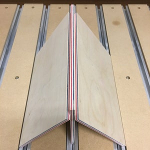 May include: A close-up of a wooden panel with red, white, and blue stripes. The panel is being cut on a CNC machine.