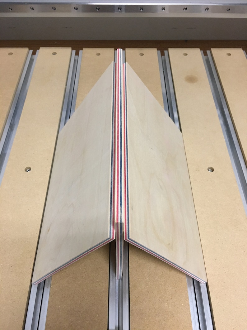 May include: A close-up of a wooden panel with red, white, and blue stripes. The panel is being cut on a CNC machine.