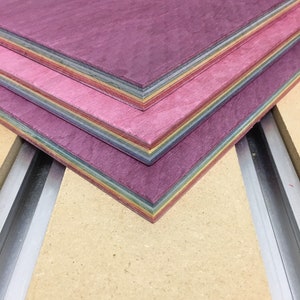 Pode incluir: Uma pilha de finas t&aacute;buas de madeira com um arco-&iacute;ris de cores sobrepostas. As t&aacute;buas s&atilde;o tingidas em tons de roxo, rosa e amarelo.