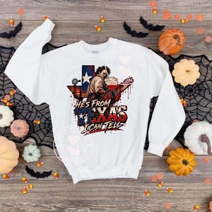Può includere: Una felpa bianca a maniche lunghe con la grafica di un personaggio che tiene una motosega davanti alla sagoma dello stato del Texas. Il testo recita HE'S FROM TEXAS I CAN TELL. Il design include schizzi rossi simili a sangue.