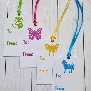 May include: Four white gift tags with different coloured ribbons and illustrations. The tags have the words "To:" and "From:" printed on them. The illustrations are a green fox, a pink butterfly, a yellow butterfly, and a blue horse.