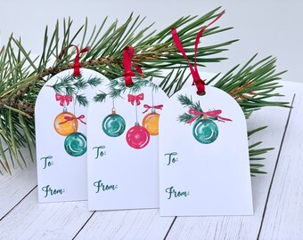 May include: Three white gift tags with a Christmas theme. Each tag features a watercolor illustration of a green pine branch with red bows and hanging ornaments in green, red, and yellow. The tags have the words "To:" and "From:" printed on them.