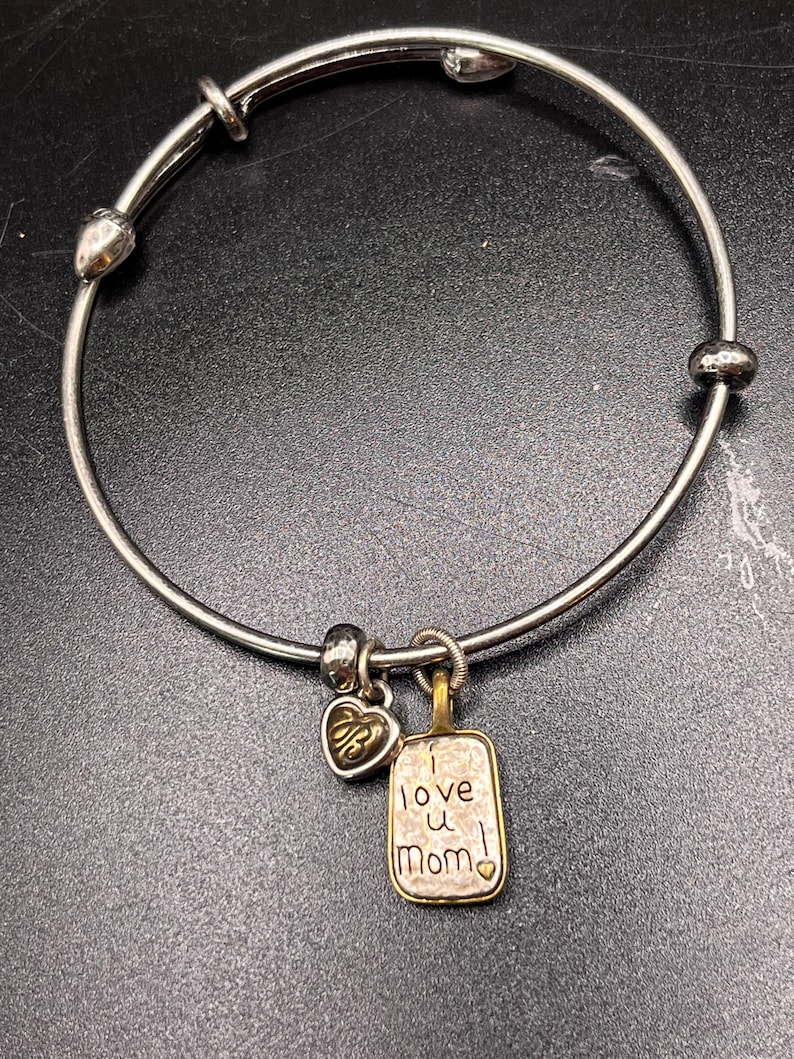 K&ouml;nnte beinhalten: Silberfarbenes Armband mit Herz- und rechteckigen Anh&auml;ngern. Der rechteckige Anh&auml;nger tr&auml;gt die Gravur "I love u Mom!". Das Armband hat einen Herzanh&auml;nger mit den Initialen "RB".