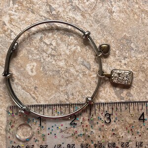K&ouml;nnte beinhalten: Silberfarbenes Armreif-Armband mit einem kleinen goldenen Herzanh&auml;nger und einem rechteckigen Anh&auml;nger mit der Gravur "love you mom". Das Armband hat einen Durchmesser von ca. 7,6 cm.