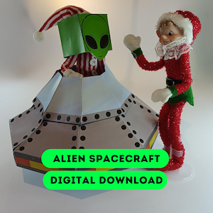 Könnte beinhalten: Eine skurrile Weihnachtsdekoration mit einem Alien in einem Raumschiff und einem Weihnachtselfen. Das Alien hat ein grünes Gesicht und befindet sich in einem silber-weißen Raumschiff. Der Elf trägt ein rotes Outfit mit weißer Verzierung. Der Text auf dem Bild lautet "ALIEN SPACECRAFT DIGITAL DOWNLOAD."