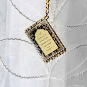 May include: A rectangular keychain with a gold chain and a decorative frame. The frame has a black background with floral accents and the text "AND HE IS WITH YOU WHERE EVER YOU ARE".
