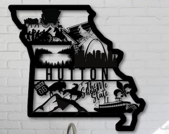 Może przedstawiać: Czarny metalowy wycinany kształt stanu Missouri z różnymi ikonami reprezentującymi stan, w tym Gateway Arch, Trasa 66, statek parowy i słowa "Show Me State".