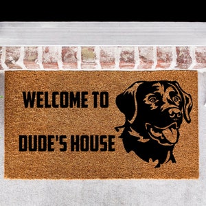 May include: A brown coir doormat with the text "Welcome to Dude's House" and a black silhouette of a Labrador Retriever's head.