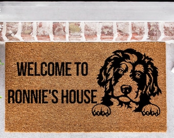 May include: A brown coir doormat with the text "Welcome to Ronnie's House" and a black silhouette of a dog peeking over the top.