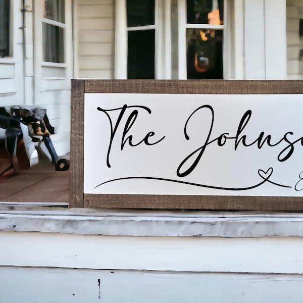 May include: A wooden sign with a white background and black text that reads "The Johnsons Est. 2025" with a small heart symbol between the words "Johnsons" and "Est."