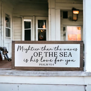 May include: A wooden sign with white paint and black lettering that reads "Mightier than the waves OF THE SEA is his love for you PSALM 93:4".