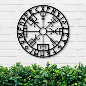 May include: Black metal wall decor featuring a circular compass design with runes and symbols. The compass is surrounded by a circle of text.