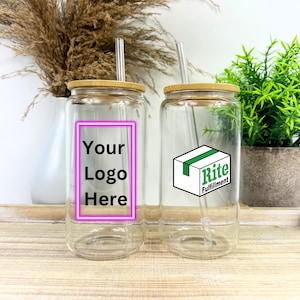 May include: Two clear glass tumblers with bamboo lids and reusable straws. One tumbler has a pink neon square with the text "Your Logo Here". The other tumbler has a white box with green trim and the text "Rite Fulfillment".