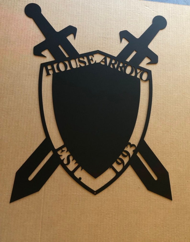 May include: Black metal shield with two crossed swords, the shield has the text "HOUSE ARROYO EST. 1993" around the edge.