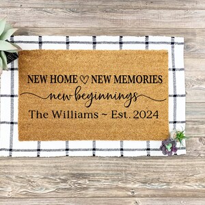 May include: A brown coir doormat with the text "NEW HOME &hearts; NEW MEMORIES new beginnings The Williams ~ Est. 2024" printed in black.