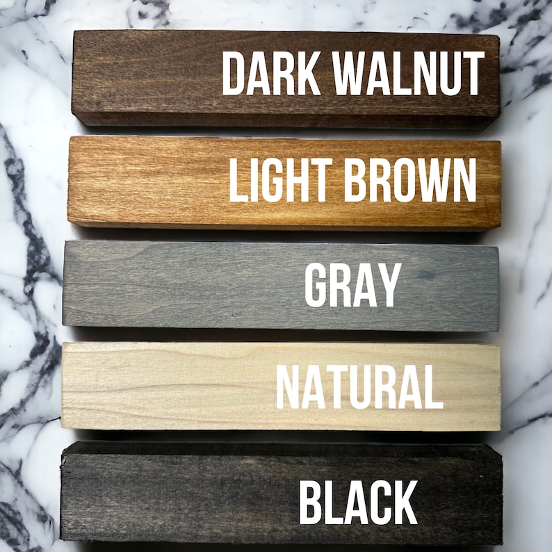 May include: Five wooden samples in different colors: dark walnut, light brown, gray, natural, and black. The wood samples are arranged vertically, with the darkest color at the top and the lightest color at the bottom.